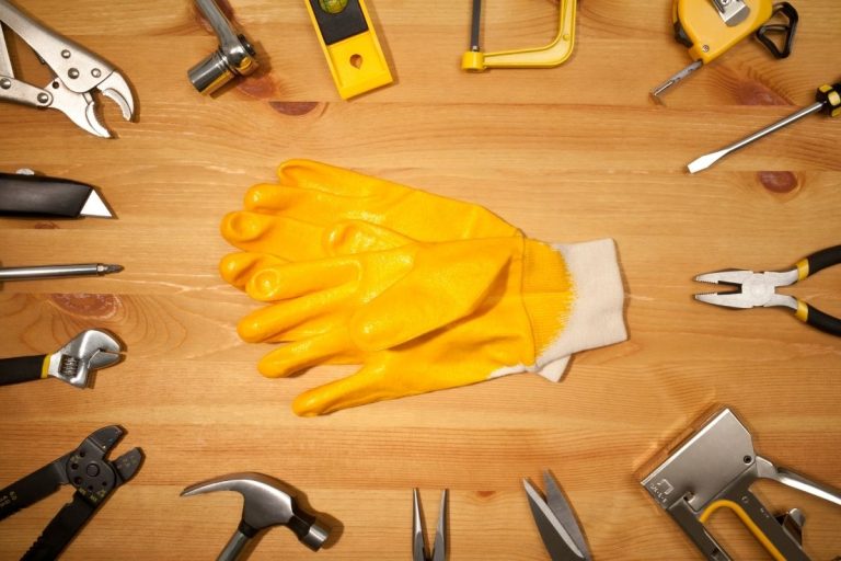 A yellow glove placed among an assortment of tools, including a hammer, screwdriver, and pliers on a workbench.